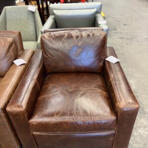 Brown leather armchair with visible wear, displayed among other chairs in a store setting.