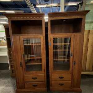 Two tall wooden cabinets with glass doors, drawers, and open shelves, displayed in a store setting.
