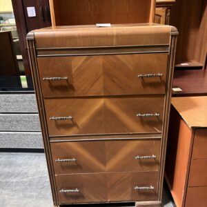 Art Deco wooden dresser with four drawers, silver handles, and chevron patterned veneer, in a secondhand store.