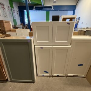 Five kitchen cabinets in a showroom, with white and gray doors, placed side by side on the floor.