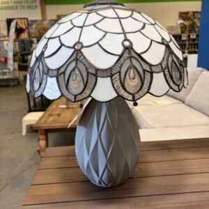 A stained glass table lamp with a decorative shade sits on a wooden table in a store.
