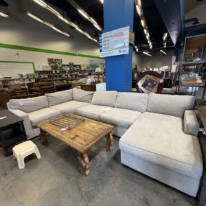Large beige sectional sofa with wooden coffee table on display in a furniture store showroom.