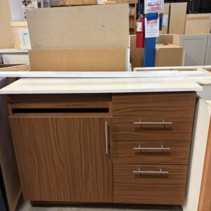 Wooden cabinet with three drawers and a white countertop in a store with other cabinets in the background.