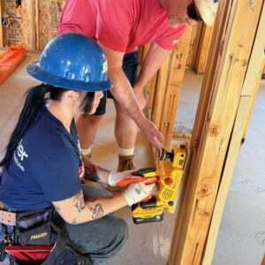Two construction workers using a power tool to measure wood framing inside a building under construction.