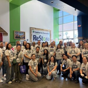 A large group of people in matching shirts pose and smile inside a Habitat for Humanity ReStore.