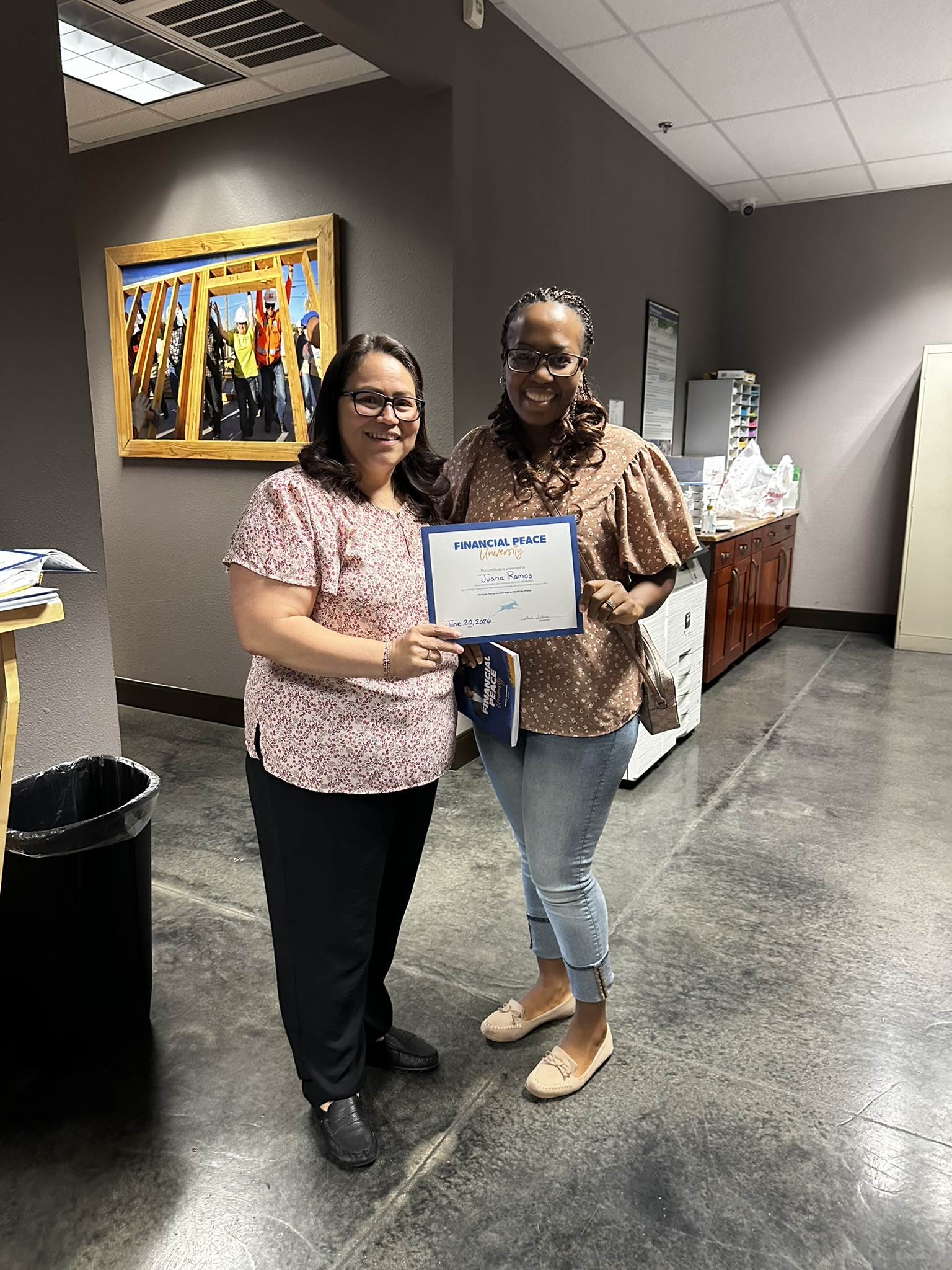 Two women smiling and holding a Financial Peace certificate in an office setting.