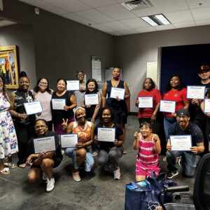Group of people indoors smiling and holding certificates, posing for a celebratory photo.