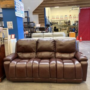 Brown leather reclining sofa displayed inside a Habitat for Humanity ReStore with other furniture in the background.