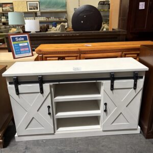White farmhouse-style TV stand with sliding barn doors on display in a furniture store.