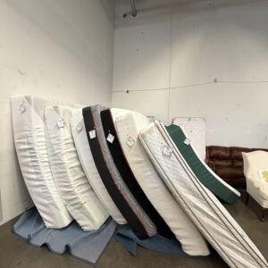 Several mattresses standing upright against a wall in a furniture store, with tags attached to each one.