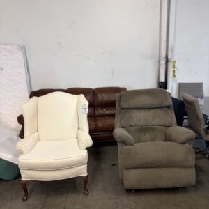 A white armchair and a brown recliner sit side by side in front of a brown couch in a warehouse.
