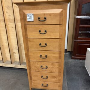 Tall wooden dresser with seven drawers and black handles, standing on a concrete floor in a store.