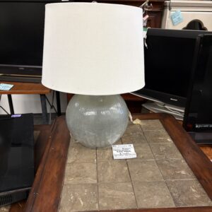 Clear glass table lamp with a white shade sitting on a wooden table, surrounded by electronics.