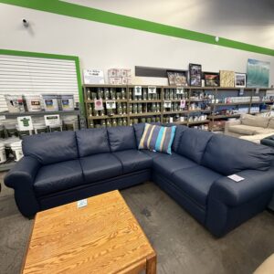 A blue sectional sofa with striped pillows next to a wooden coffee table in a store showroom.