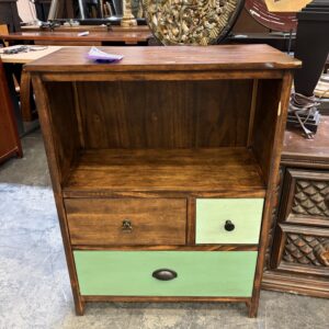 A wooden cabinet with an open shelf and three drawers, two painted green, on a concrete floor.