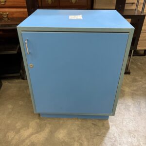 A blue metal cabinet with a single door and a lock, standing on a concrete floor indoors.