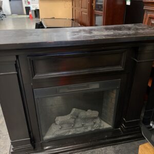 A dark wooden electric fireplace with a glass front and faux logs, placed in a store or warehouse.
