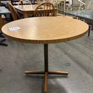 Round wooden table with a single pedestal base, displayed among other furniture in a store.