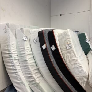 Several mattresses are standing upright in a row, each with a price tag attached, against a white wall.