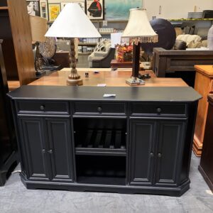 Black sideboard with two table lamps on top, displayed in a furniture store with art on the wall behind.