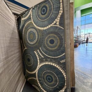 Large rug with a circular geometric pattern in blue, cream, and gold displayed in a store.