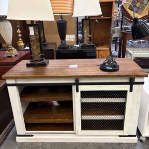 Wooden console with lamps on top, open shelves, and a sliding wire mesh door, in a furniture store.