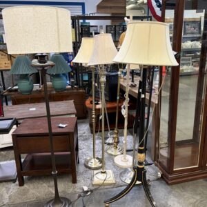 Five assorted floor lamps with fabric shades are displayed among wooden furniture in a store setting.