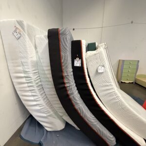 Five mattresses leaning upright against a wall, each with a price tag attached, in a showroom.