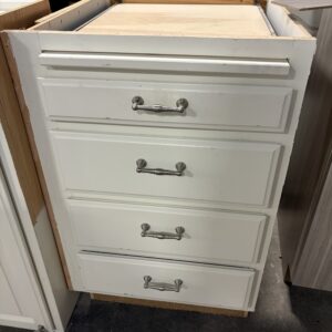 White cabinet with four drawers and silver handles, missing the countertop, placed on a concrete floor.