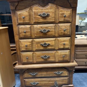Tall wooden dresser with ornate handles and carved details, placed on a blue floor in a store.