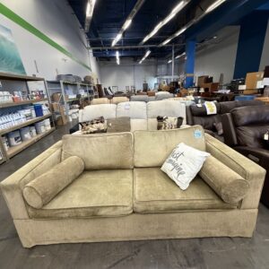 Beige sofa with bolster pillows and decorative cushions in a large furniture store showroom.