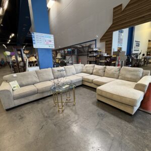 Large beige sectional sofa with glass-top tables in a spacious showroom with blue pillars and high ceilings.