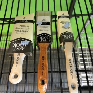 Three BEST LOOK paintbrushes in packaging displayed upright on a black metal shelf with green background.