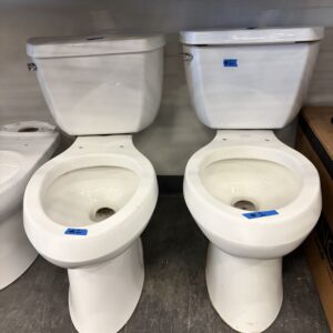 Two white toilets sit side by side on a showroom floor, yellow caution tape above them.