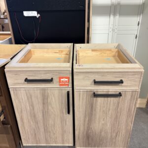 Two light wood bathroom vanities side by side, without sinks, on a showroom floor.