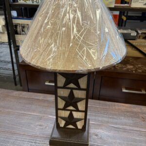 Table lamp with star design on base, wrapped lampshade, sitting on a wooden surface in a store setting.