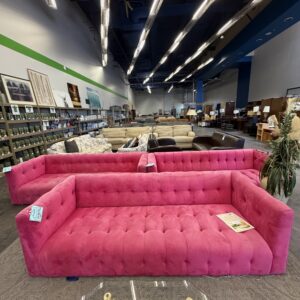 Bright pink tufted sofa on display in a furniture store with various couches and shelves in the background.