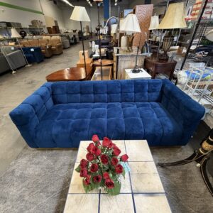 Blue velvet couch with a marble coffee table and a vase of red roses in a furniture store.