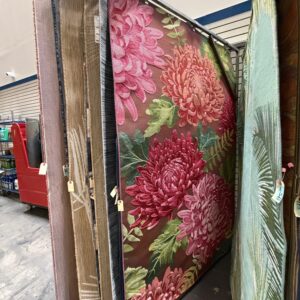 Area rugs on display, including one with large pink flowers and green leaves in a store aisle.