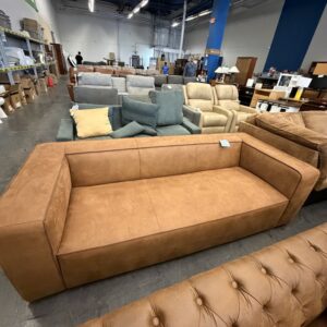 Brown suede sofa in a furniture showroom, surrounded by other couches, chairs, and shelves.