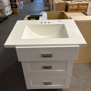 White bathroom vanity with three drawers and integrated sink on display in a warehouse store.