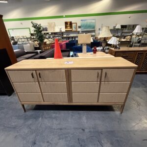 Light wood sideboard with cabinets, a red cone, and various lamps on top in a furniture store.
