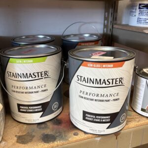 Three cans of STAINMASTER Performance interior paint and primer on a shelf, labeled satin and semi-gloss.