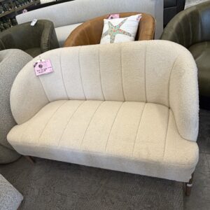 Cream-colored loveseat with rounded backrest on display in a furniture store, with other sofas nearby.