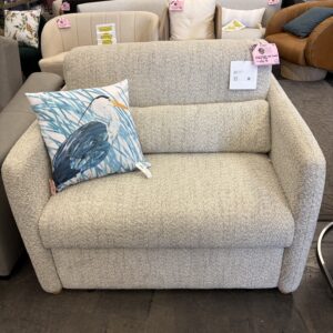 Small beige loveseat with a blue heron pillow, displayed in a furniture store.