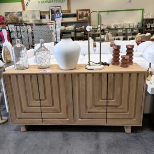 Wood cabinet with geometric design topped with vases, a lamp, and decor items in a store setting.