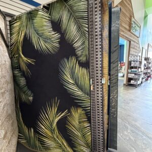 Large rugs with various patterns, including palm leaves, displayed upright in a store aisle.