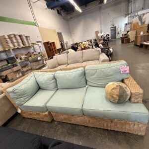 Wicker sectional sofa with light blue cushions and a round pillow in a warehouse furniture store.
