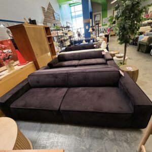 A large, black sectional sofa is displayed in a furniture store with other home items and decor around it.