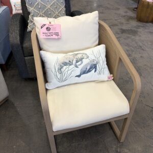 Beige wooden chair with cream cushions and a decorative pillow featuring two manatees in water plants.